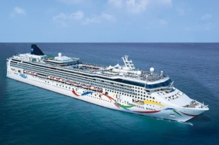 Aerial view of Norwegian Dawn cruise ship with colours swirling along the side of the ship featuring calm blue seas and clear skies