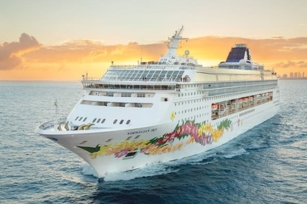 Image of the front of Norwegian Sky as the sun sets there is an orange hue in the sky